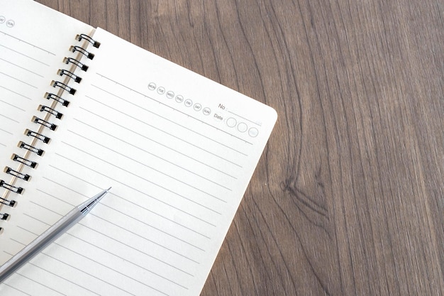 Vue de dessus d'une page de cahier ouvert vierge et d'un crayon sur fond de table en bois au bureau