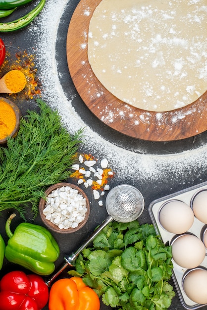 Vue de dessus de la pâte circulaire sur une planche de bois ronde avec de la farine autour et des épices de légumes frais