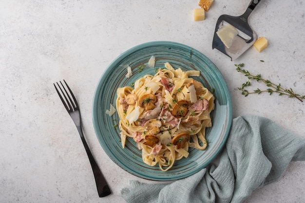 Vue de dessus pâtes fettuccine aux champignons, bacon, parmesan en assiette blanche avec fourchette