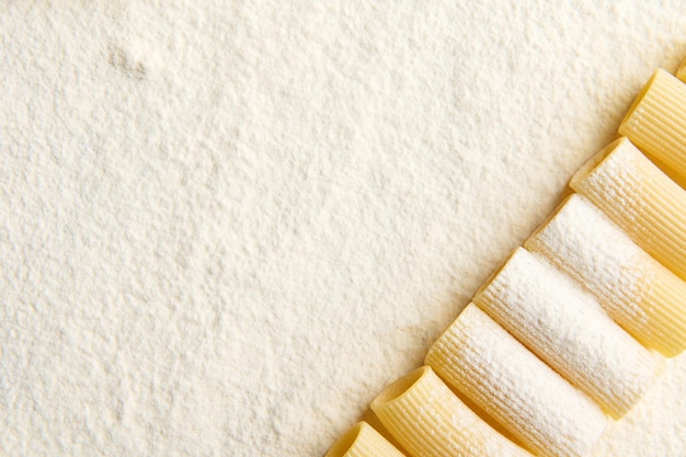 Vue de dessus de pâtes italiennes de blé entier soigneusement disposées dans une rangée au coin d'une surface farinée avec espace de copie pour la publicité