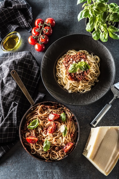 Vue de dessus des pâtes italiennes spaghetti bolognaise dans une assiette et une poêle avec des tomates et du basilic.