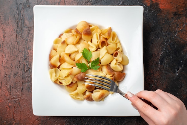 vue de dessus des pâtes savoureuses sur une fourchette à assiette dans une main de femme sur une table en bois