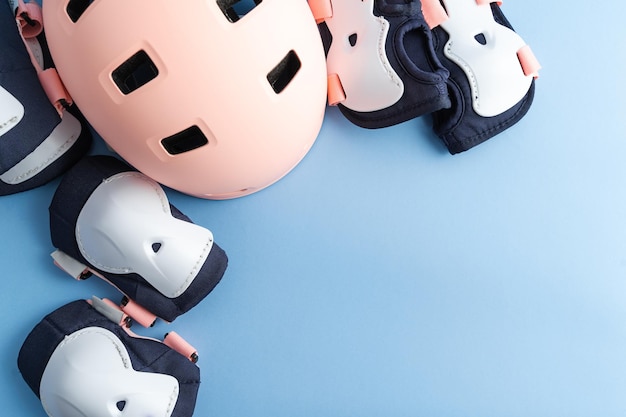 Vue de dessus des patins à roulettes ensemble d'équipements de protection coudières et protège-poignets et casque dans des couleurs roses fond bleu mise à plat