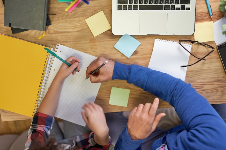 Photo vue de dessus d'un père latin attentionné aidant son fils à faire ses devoirs expliquant la tâche de prendre des notes
