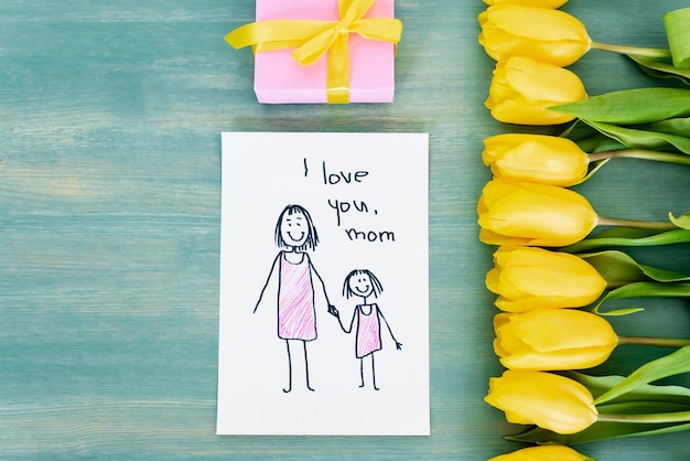 Vue de dessus de la petite boîte-cadeau près de la carte de voeux avec je t'aime maman lettrage et tulipes jaunes sur