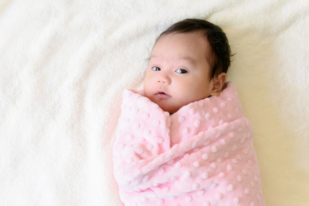 Vue de dessus d'une petite fille asiatique mignonne enveloppée dans un tissu rose allongé sur le lit