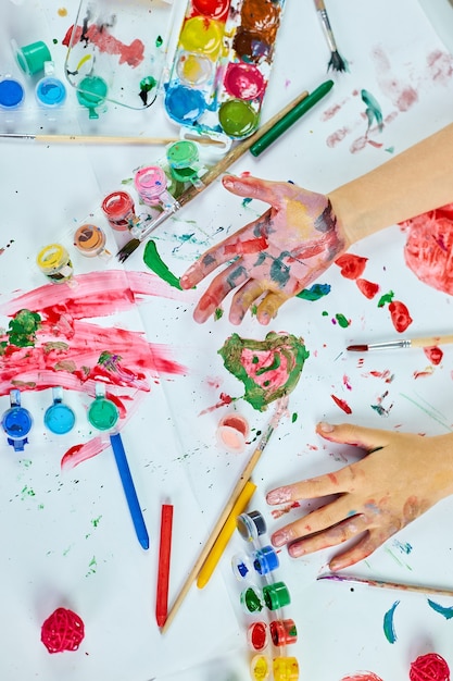 Vue de dessus Petite fille aux mains aquarelles colorées peintes, enfant assis à la table et dessinant, concept d'école d'art, fille enfant peignant à la maison