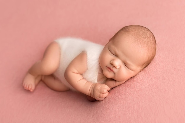 Vue de dessus d'une petite fille nouveau-née dormant dans une salopette blanche sur fond rose Beau portrait d'un nouveau-né 7 jours sur 7