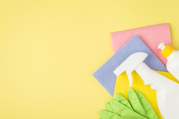 Vue de dessus photo de bouteilles en plastique de détergent en spray et en gel trois chiffons de viscose multicolores et des gants en caoutchouc vert sur fond jaune isolé avec espace pour copie