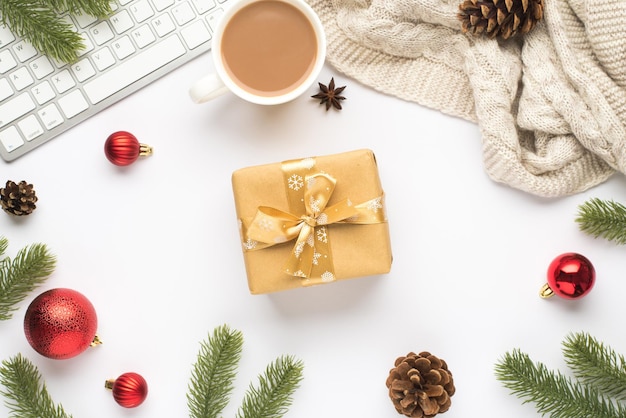 Vue de dessus photo de clavier tasse de boisson chaude boules de sapin de Noël rouge brindilles de pin cônes écharpe d'anis et boîte-cadeau avec arc d'or sur fond blanc isolé