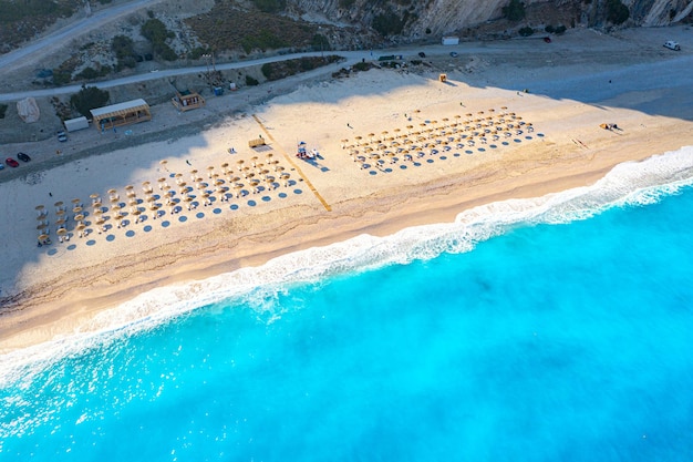 Vue de dessus photo de drone aérien de la plage de Myrtos avec de belles vagues de mer turquoise et des parapluies de paille Fond de voyage de vacances Mer Ionienne Île de Céphalonie Grèce