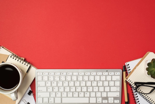 Vue de dessus photo du clavier blanc du lieu de travail piles d'organisateurs lunettes clips de reliure plante stylo et tasse de café sur fond rouge isolé avec espace vide