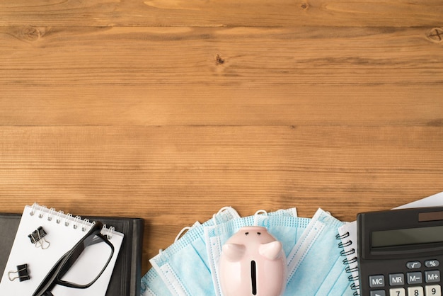 Vue de dessus photo du lieu de travail avec des masques de lunettes de calculatrice organisateurs noirs et tirelire sur fond de table en bois isolé avec fond