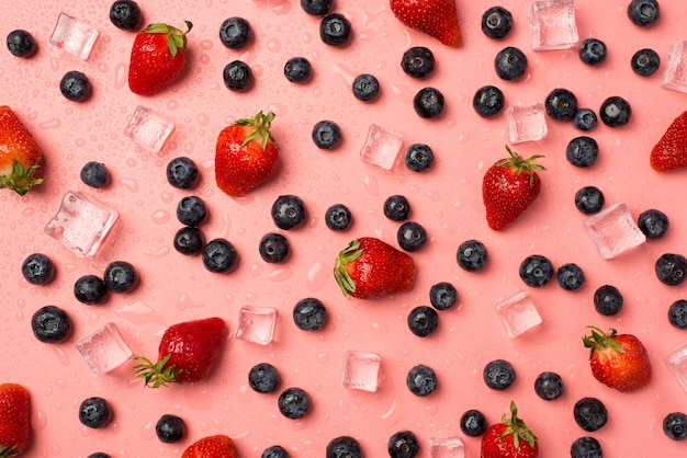 Vue de dessus photo de fraises éparses avec des feuilles de glaçons de bleuets et de gouttes d'eau sur fond rose clair isolé