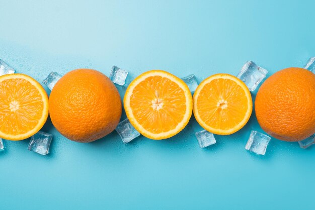 Vue de dessus photo d'oranges coupées et entières et de glaçons crus sur fond bleu pastel isolé avec espace pour copie