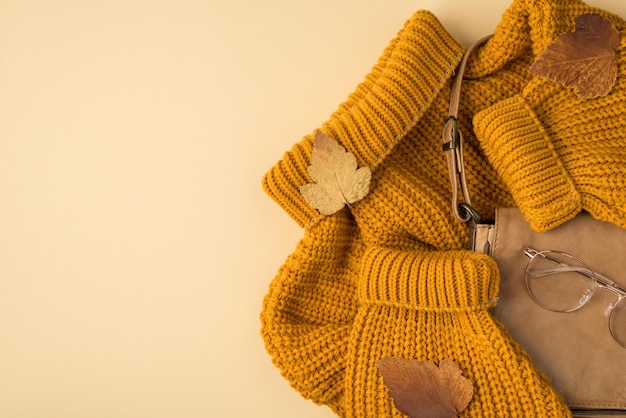 Vue de dessus photo de sac en cuir chandail jaune lunettes élégantes et feuilles brunes d'automne sur fond beige clair isolé avec espace pour copie