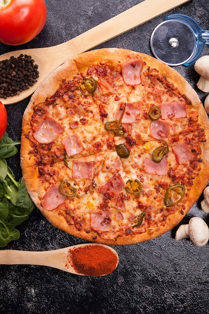 Vue de dessus sur la pizza chaude à côté des ingrédients dont elle est faite sur une planche en bois sombre