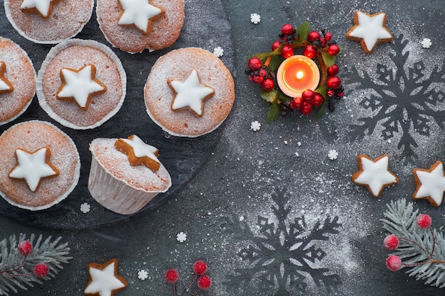 Vue de dessus de la planche de bois avec des muffins saupoudrés de sucre, du glaçage au fondant et des biscuits étoile de Noël