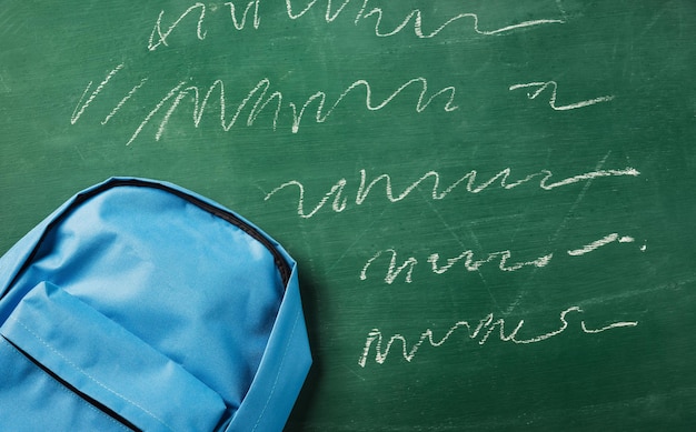 Vue de dessus à plat du sac à dos bleu cartable sur un tableau vert et espace de copie pour votre texte, concept d'éducation de retour à l'école
