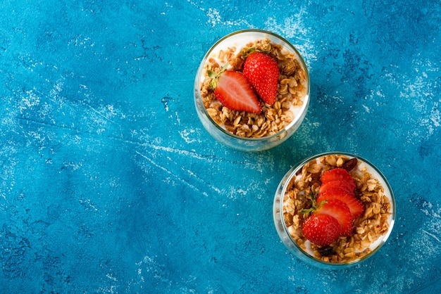 Vue de dessus, plat poser deux tasses en verre avec dessert aux fruits et baies de mangue et fraises avec granola et crème à la vanille ou ricotta