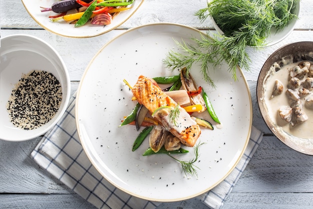 Vue de dessus d'un poisson saumon cuit à la vapeur sain et de légumes à côté d'herbes et de sauce aux champignons.