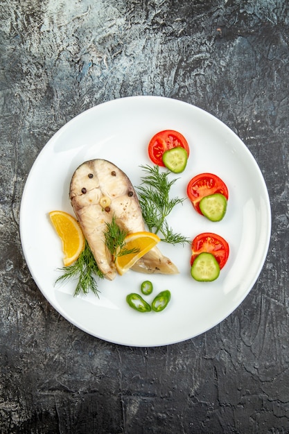 Vue de dessus des poissons crus et des aliments frais au poivre sur une plaque blanche sur une surface de glace grise