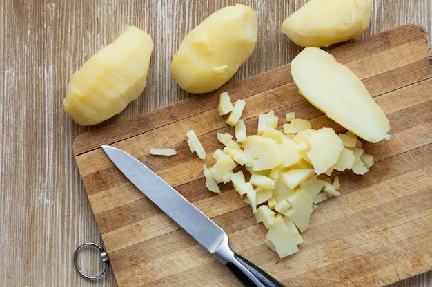 Vue de dessus des pommes de terre bouillies frottées coupées dans des vestes à l'aide d'un couteau sur le fond en bois