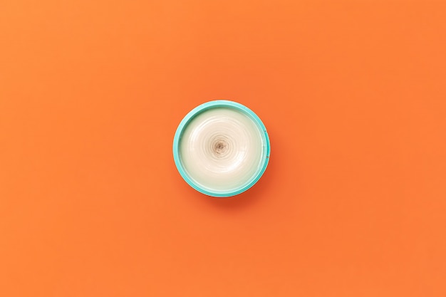 Vue de dessus sur un pot lumineux de couleur turquoise avec de la crème cosmétique sur une orange. Le concept de la beauté, de la médecine, des soins de la peau du visage et du corps, des soins capillaires