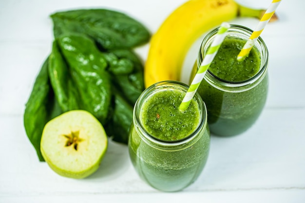 Vue de dessus des pots de verres remplis de smoothie vert et d'ingrédients sur une table en bois