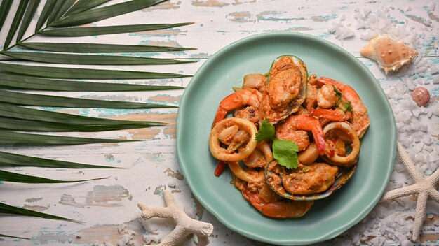 Vue de dessus de la poudre de curry sauté de fruits de mer sur plaque en céramique verte sur table en bois, cuisine thaïlandaise