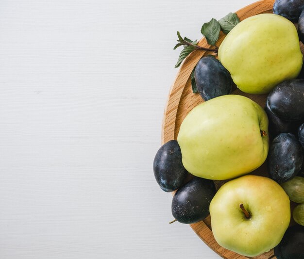 Vue de dessus des prunes et des pommes dans la plaque en bois