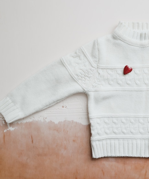 Vue de dessus Pull en laine blanche avec un coeur rouge. Mise à plat