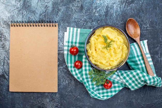 Vue de dessus de purée de pommes de terre servie avec une cuillère en bois d'aneth tomates fraîches sur une serviette verte et un cahier sur fond de couleur sombre avec espace libre