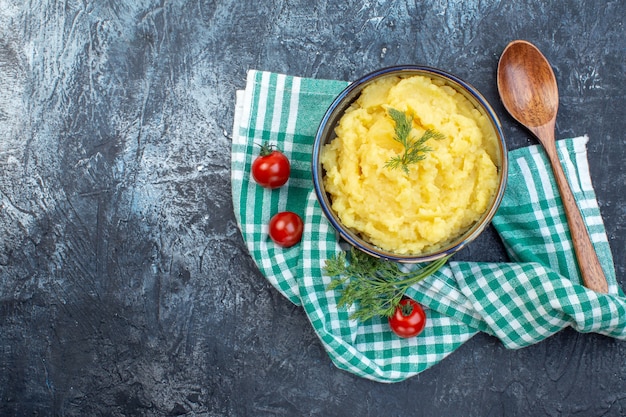 Photo vue de dessus de la purée de pommes de terre servie avec une cuillère en bois à l'aneth tomates fraîches sur une serviette verte sur le côté gauche sur fond de couleur sombre avec espace libre