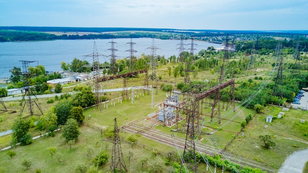 Vue De Dessus Des Pylônes électriques Et Des Lignes à Haute Tension Sur L'herbe Verte Sur Le Fond De La Rivière.