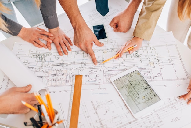 Vue de dessus de quatre architectes à succès examinant des plans et utilisant une tablette numérique. Fermer.