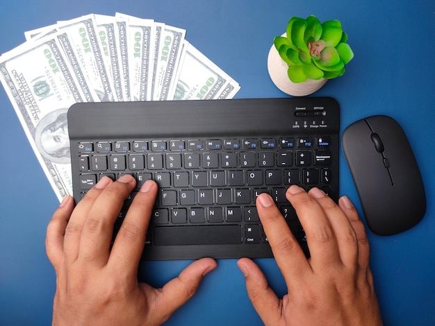 Vue de dessus quelqu'un tapant à la main un clavier sans fil avec des billets sur fond bleu