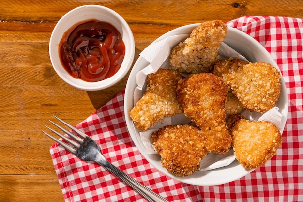 Vue de dessus de quelques pépites de poulet frites dans un bol blanc accompagnées de sauce kétchup sur une table