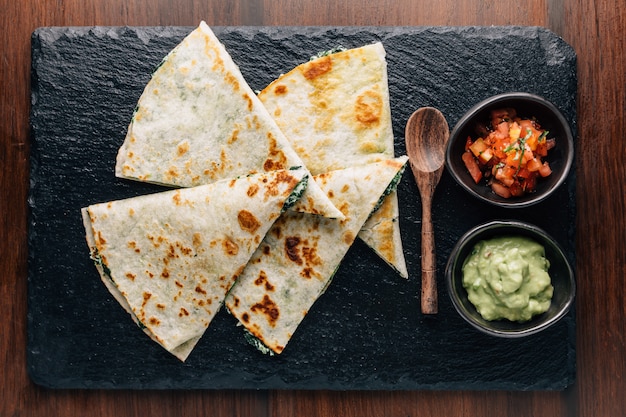 ฺ Vue de dessus de quesadillas aux épinards et au fromage cuits au four, servis avec salsa et guacamole.