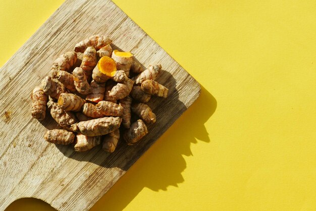 vue de dessus de la racine de curcuma sur une planche à découper sur fond jaune