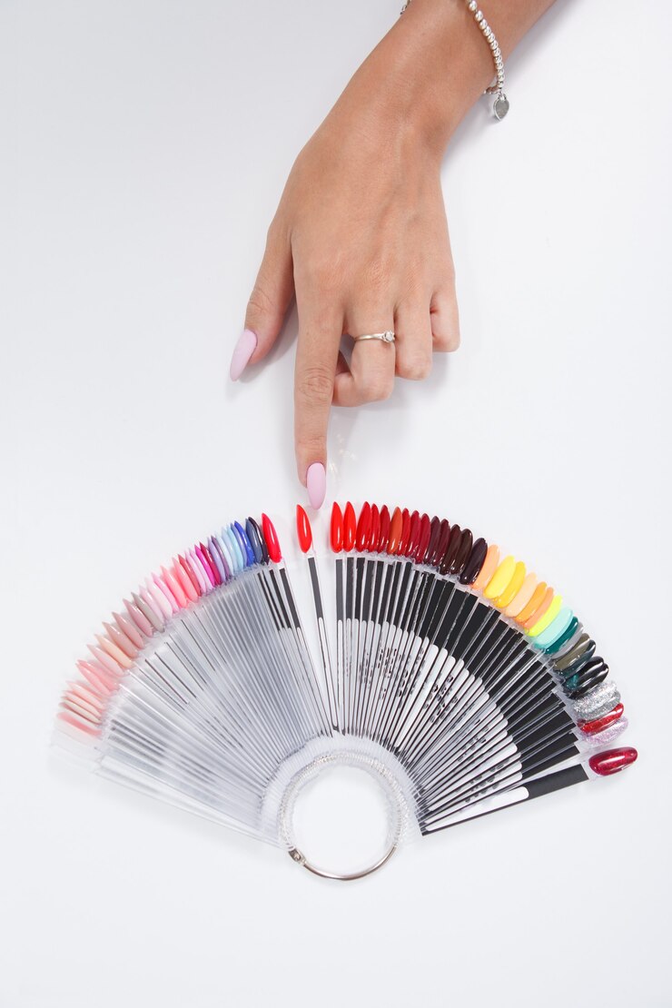 Vue de dessus recadrée d'une main féminine pointant sur une couleur sur une palette de vernis à ongles