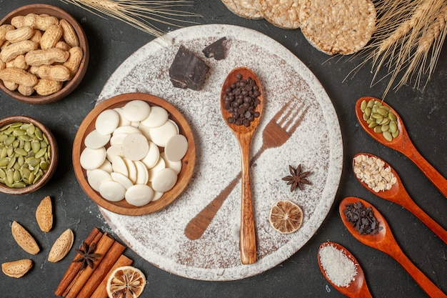 vue de dessus des ronds de chocolat blanc dans un bol en bois empreinte de fourche avec du sucre glace des cuillères en bois des bâtons de cannelle sur une assiette sur une table