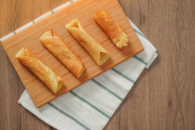 Vue de dessus, rouleau de crêpes rempli de saveurs assorties sur une planche à découper en bambou placé sur un tissu rayé blanc et vert sur une table en bois