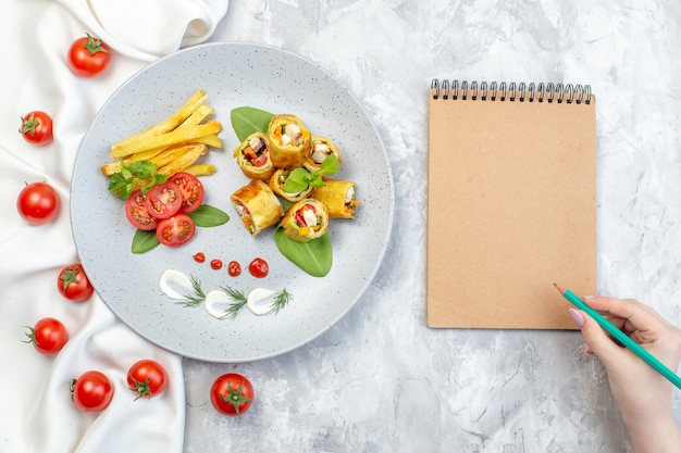 Vue de dessus des rouleaux de pâté de légumes avec des tomates et des frites à l'intérieur de la plaque sur une surface blanche