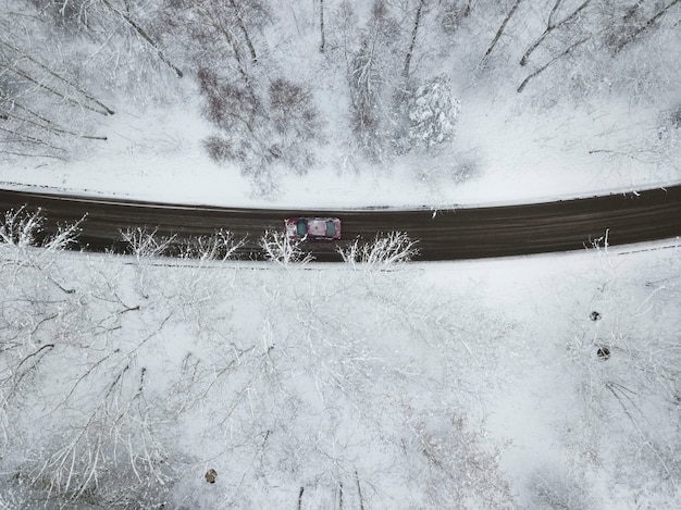 Vue de dessus de la route à travers la forêt couverte de neige sur laquelle la voiture roule