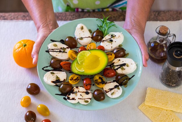 Vue de dessus de la salade caprese fraîche Les mains des femmes tiennent une assiette avec de la mozzarella au fromage et de petites tomates