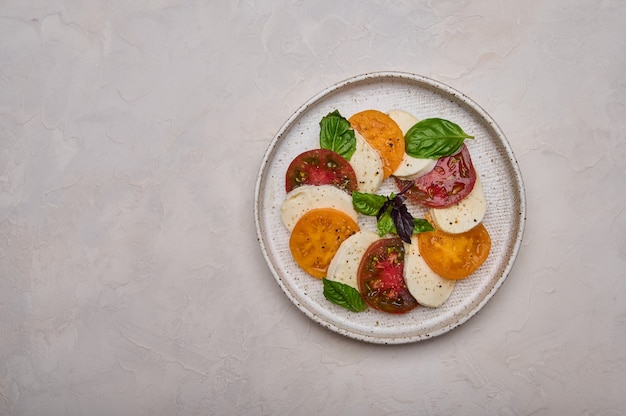 Vue de dessus salade caprese avec tomates rouges et jaunes, basilic frais et fromage mozzarella dans une assiette blanche