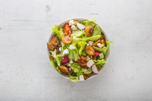 Vue de dessus de la salade de légumes avec des morceaux de poulet sur fond de béton blanc.