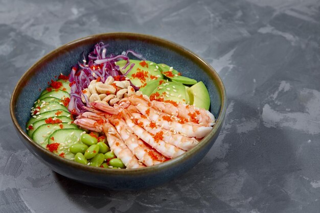 Vue de dessus sur la salade poke aux crevettes rouges et légumes verts dans les bols sur fond gris Espace de copie