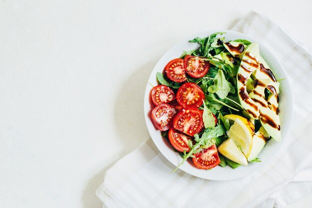 Vue de dessus de la salade de tomates roquette avocat citron en plaque blanche sur fond clair